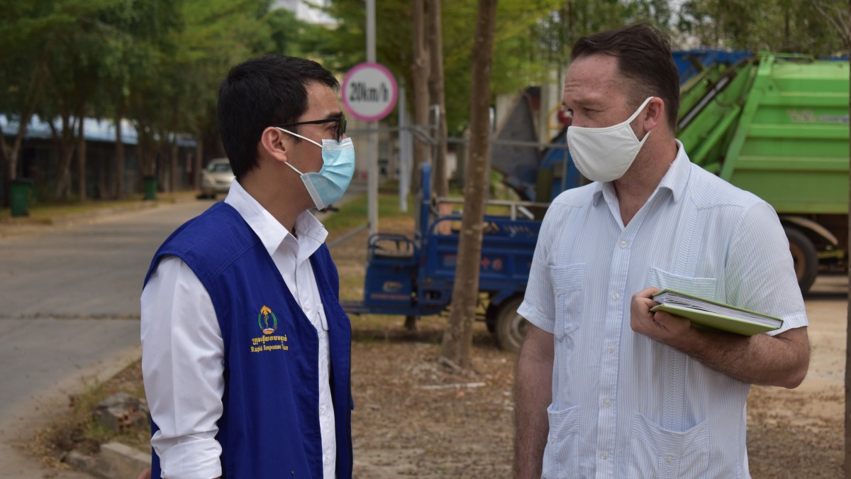 Two men wearing masks talk to each in a street in Cambodia.