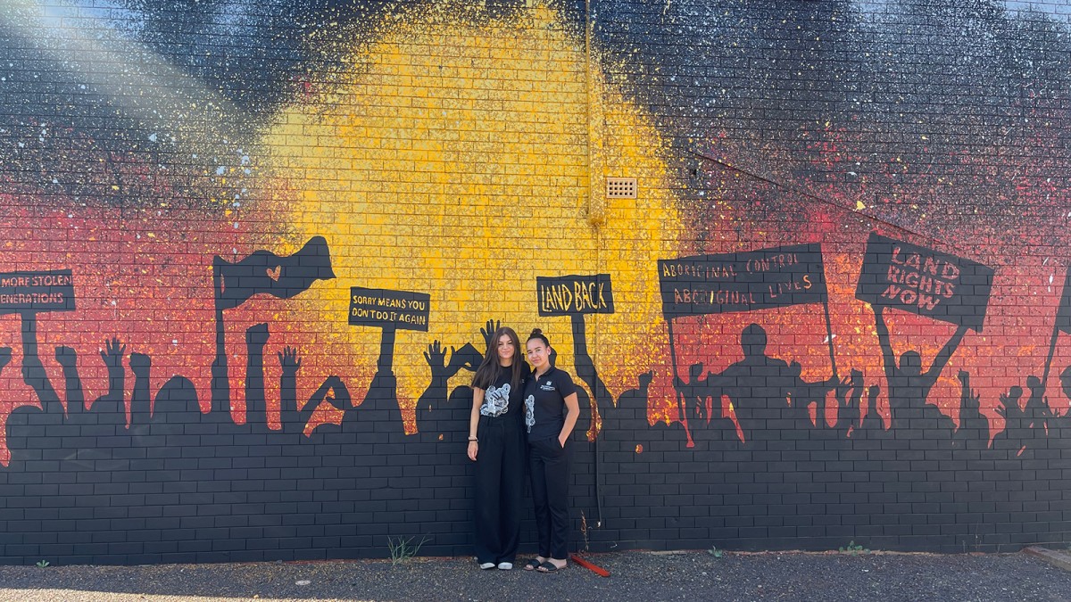 Project officers Tasha Cole and Taleah Carson in front of an Indigenous mural. 