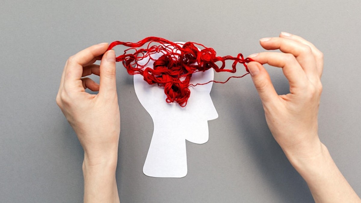 A paper silhouette of a head and two hands untangling red wool on the paper, symbolising the brain 