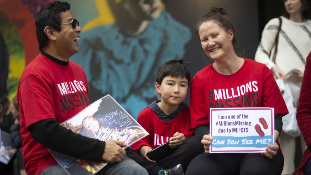 Protest for ME/CFS health equality featuring a man, woman and child holding up sign with: I am one of the #MillionsMissing due to ME/CFS.