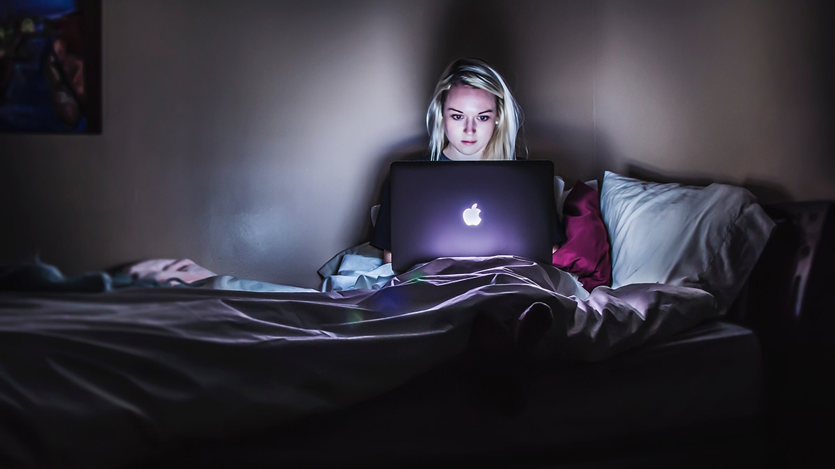 Worried girl looks at her computer in bed.